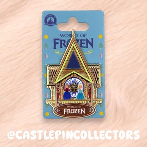 以下が含まれることがあります： 「WORLD OF FROZEN」の文字が入った時計台のデザインのピンバッジ。 金、青、赤のアクセントがあり、アナとエルサのキャラクターが描かれています。 ピンバッジは青色の台紙に付いています。