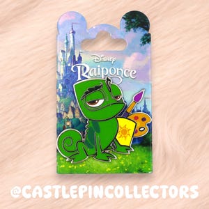 Puede incluir: Un pin de esmalte de Disney Rapunzel con Pascal el camaleón con un pincel y una paleta. El pin es verde, amarillo y morado, sobre un fondo de un castillo y cielo. El pin está en una tarjeta con el texto "Rapunzel".