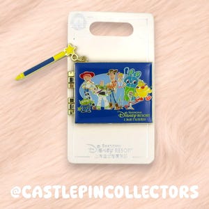 May include: A Disney pin featuring characters from Toy Story, including Woody and Buzz Lightyear, on a blue background. The pin has a gold-coloured wand charm with a yellow star. The pin is attached to a white backing card.