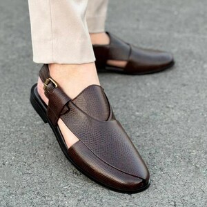 May include: Brown leather sandals with a textured finish. The sandals feature a slingback strap with a gold-colored buckle and a cutout design on the sides. The sole is black.