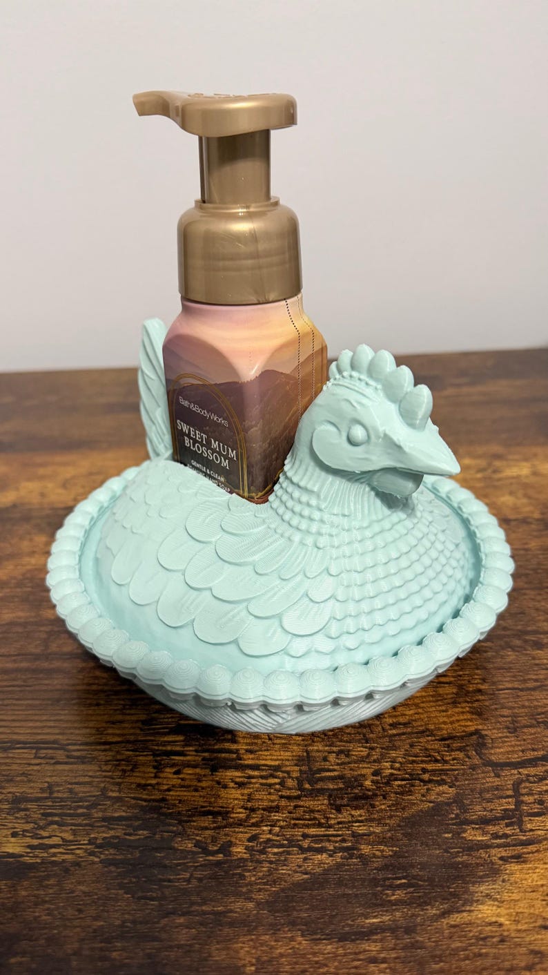 Peut inclure: Un porte-savon en forme de poulet bleu clair avec une bouteille de savon Sweet Mum Blossom. Le support pr&eacute;sente un design d&eacute;taill&eacute; et une pompe dor&eacute;e. La bouteille de savon porte une &eacute;tiquette avec un paysage.