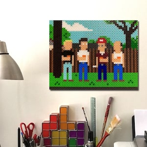 Peut inclure: Une impression sur toile en pixel art représentant quatre personnages dans un parc. L'œuvre présente une pelouse verte, un ciel bleu et des arbres bruns. L'impression est affichée au-dessus d'un bureau avec une lampe, des tasses et des blocs géométriques colorés.