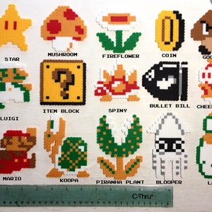 Puede incluir: Una colecci&oacute;n de personajes y objetos de pixel art de la serie de videojuegos Super Mario. Incluye a Mario, Luigi, una estrella, una seta, una flor de fuego, una moneda, Goomba, Bullet Bill, Cheep Cheep, un bloque de objetos, Spiny, Koopa, Piranha Plant, Blooper y Lakitu.