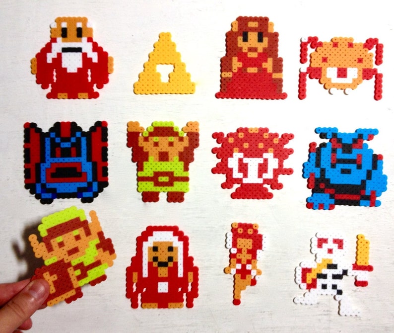 May include: A collection of colorful pixel art characters from a video game. The characters are made from small, fused plastic beads. The characters include a wizard, a princess, a triangle, and various monsters.