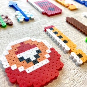 Puede incluir: Una colecci&oacute;n de creaciones de arte pixelado coloridas, que incluyen una guitarra, una llave y una espada, hechas de peque&ntilde;as cuentas de pl&aacute;stico. Los dise&ntilde;os presentan varios colores como verde, azul, marr&oacute;n y rojo, dispuestos sobre una superficie clara.