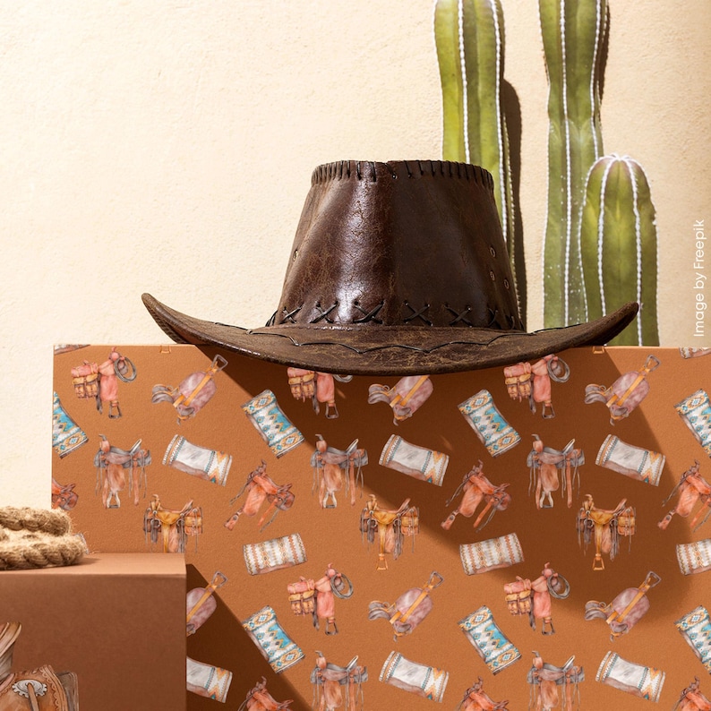 May include: A brown leather cowboy hat with a stitched brim sits atop a patterned surface. The surface features a repeating watercolor design of saddles, horses, and other western elements. Green cacti stand in the background.