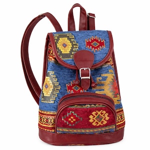 May include: A blue backpack with a colorful woven pattern and burgundy leather trim. The bag features a front pocket, adjustable straps, and a buckle closure. The woven design includes yellow, red, and blue geometric shapes.