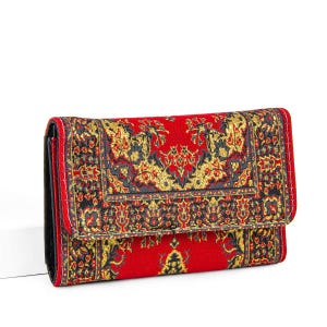 Könnte beinhalten: Eine rote Geldbörse mit einem detaillierten, verzierten Muster in Gold, Schwarz und Rot. Die Geldbörse hat eine Klappe und ein schwarzes Innenfutter. Das Design ähnelt einem traditionellen Teppich.
