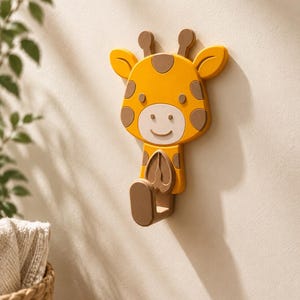 May include: A yellow giraffe-shaped wall hook with brown spots, ears, and a hook. The giraffe has a smiling face and is mounted on a beige wall. The hook is designed for hanging items and adds a playful touch to any room.