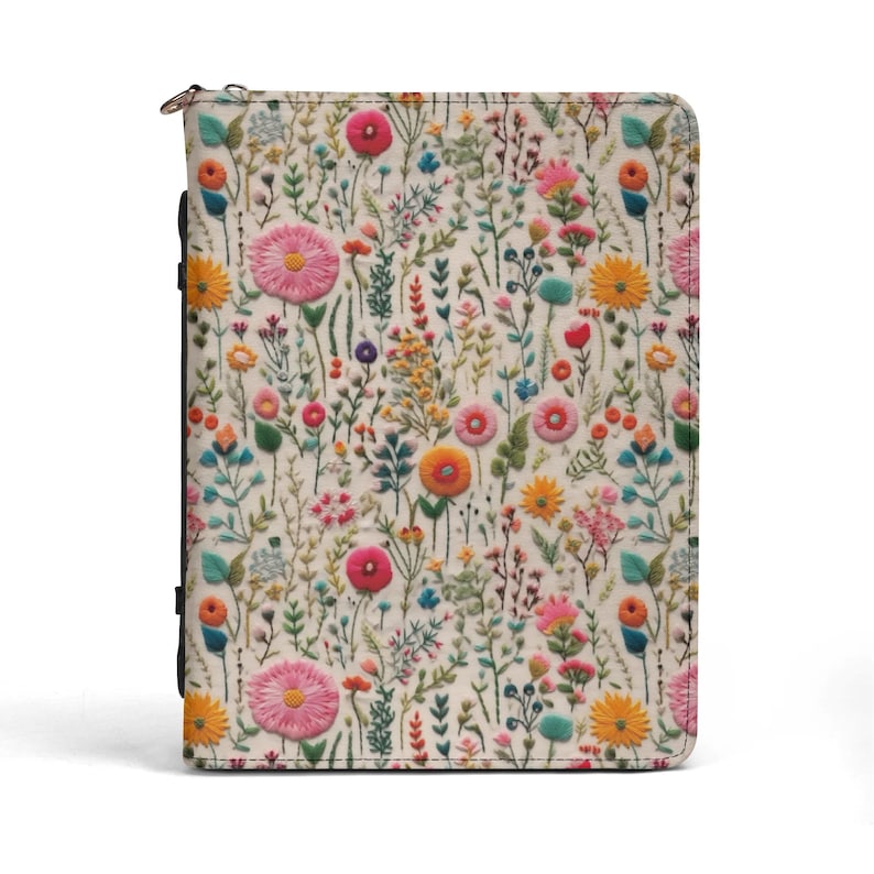 May include: A rectangular zippered binder featuring an off-white background with a dense, colorful pattern of embroidered-style wildflowers, including pink, yellow, orange, and blue blossoms, stems, and leaves across the entire front surface.