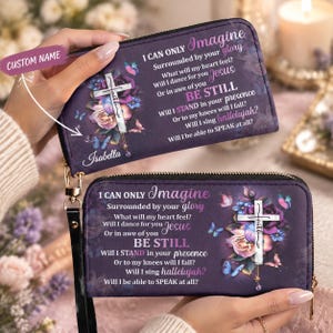 May include: A rectangular purple wallet with a wrist strap featuring a floral design, a cross with the word faith, and the text I CAN ONLY Imagine Surrounded by your glory What will my heart feel? Will I dance for you Jesus Or in awe of you BE STILL Will I STAND in your presence Or to my knees will I fall? Will I sing hallelujah? Will I be able to SPEAK at all? The name Isabella is printed on the front.