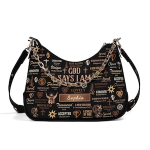 May include: A black hobo bag featuring a gold-toned chain strap and a repeating pattern of religious text, crosses, and symbols. The center displays the text "GOD SAYS I AM" above a rectangular nameplate with the name "Sophia" in gold lettering.