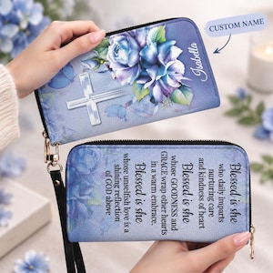 May include: A blue wallet featuring a floral print of blue roses and a white cross on the front. The back displays the text: Blessed is she who daily imparts nurturing care and kindness of heart. Blessed is she whose GOODNESS and GRACE wrap other hearts in a warm embrace. Blessed is she whose unselfish love is a shining reflection of GOD above. The name Isabella is printed on the front.