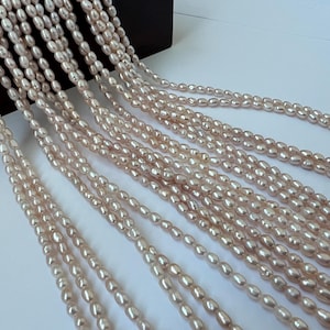 Puede incluir: Múltiples hebras de perlas de agua dulce de color rosa claro caen desde una superficie oscura. Las perlas ovaladas tienen un brillo sutil. La imagen muestra la delicada belleza de las perlas, ideales para la creación de joyas o manualidades.