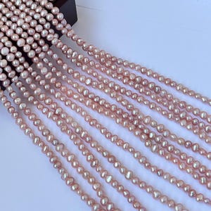 May include: Strands of pink freshwater pearls of varying sizes. The pearls have a lustrous sheen and are strung together, creating a delicate and elegant appearance. The pearls are a soft, natural pink color.
