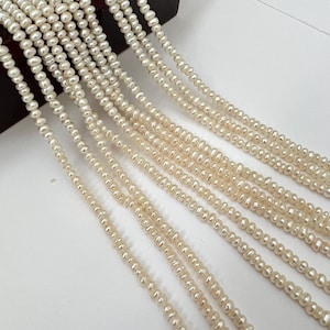May include: Multiple strands of creamy white freshwater pearls. The pearls are small and irregularly shaped, strung together to create a delicate and elegant look. The background is a light, neutral color.