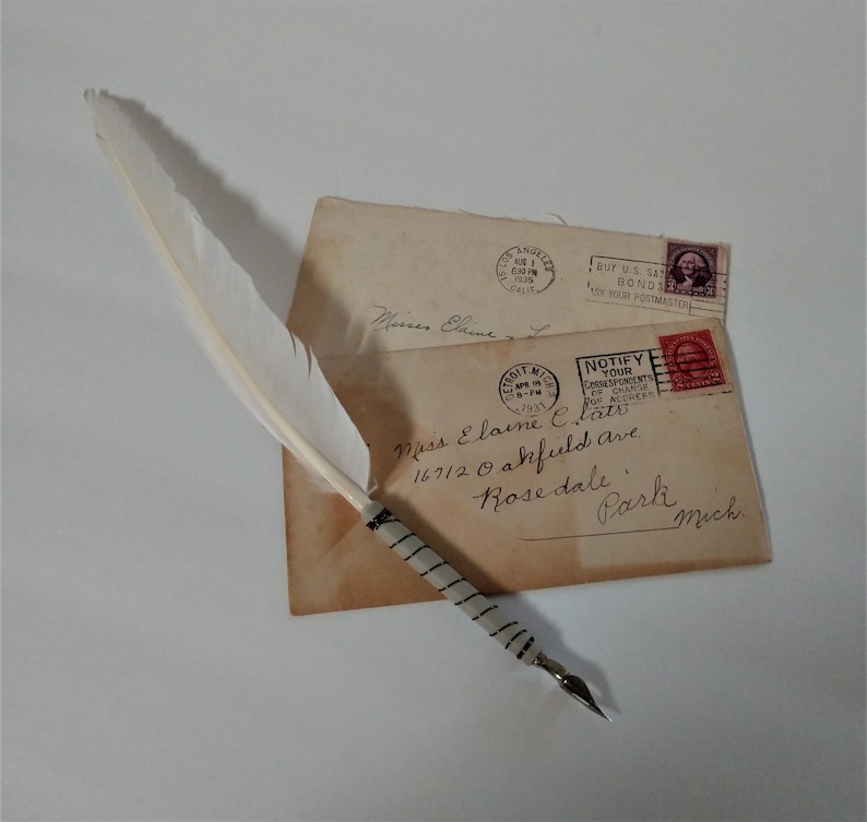 May include: A white feather quill pen with a black and white striped handle resting on top of two envelopes. The envelopes are addressed to Miss Elaine C. Clats, 16712 Oakfield Ave, Rosedale Park, Mich. The envelopes have stamps from the United States Postal Service.