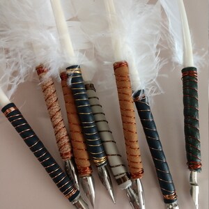May include: A set of eight white feather quill pens with different colored wrappings. The wrappings are made of leather and copper wire. The quills have metal nibs.
