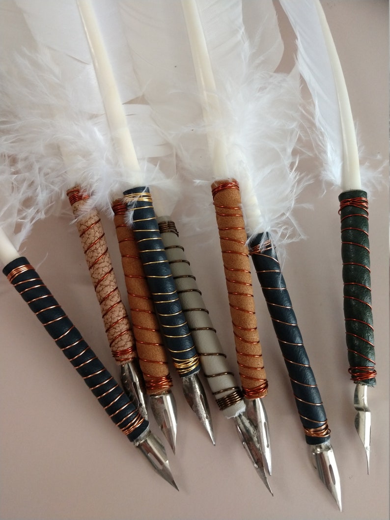 May include: A set of eight white feather quill pens with different colored wrappings. The wrappings are made of leather and copper wire. The quills have metal nibs.