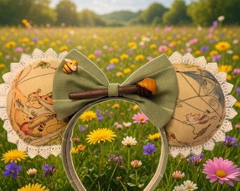 Puede incluir: Una diadema caprichosa con orejas temáticas de Winnie the Pooh. Las orejas presentan una tela beige con ilustraciones, ribete de encaje blanco y un lazo verde con adornos de cuchara de miel y abeja. La diadema se coloca contra un campo vibrante de flores silvestres.