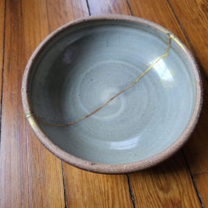 Pode incluir: Um conjunto de três canecas de cerâmica com acabamento fosco e salpicado. As canecas são em tons de creme, cinza claro e cinza escuro. Cada caneca tem um design simples e minimalista.