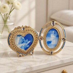 May include: Two gold-toned metal picture frames with blue enamel accents and clear rhinestones. One frame is heart-shaped with a 2.5 inch by 2.5 inch opening, and the other is oval-shaped with a 2 inch by 3 inch opening, both featuring clear crystals.