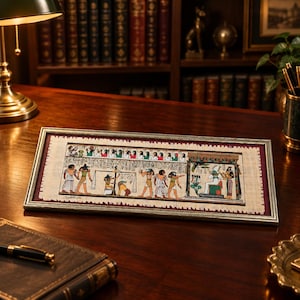 May include: A rectangular framed papyrus painting featuring a detailed scene of ancient Egyptian figures, including deities with animal heads, hieroglyphics, and a weighing of the heart ceremony, set against a dark red matting in a silver frame.