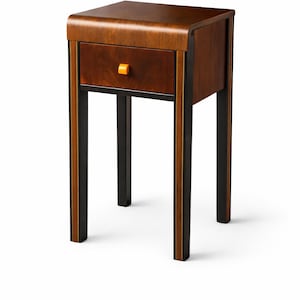 May include: A wooden nightstand with a curved top and a single drawer. The nightstand is primarily brown with black and gold accents on the legs. The drawer has an orange knob. A stylish piece of bedroom furniture.