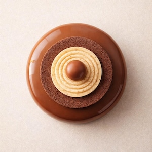 Op de afbeelding: Een gelaagd dessert met een glanzende, donkerbruine buitenlaag, een getextureerde bruine middenlaag en een lichtgekleurd, cirkelvormig centrum met concentrische ringen. Een kleine, ronde chocoladebal ligt erbovenop. Het dessert staat op een lichtbeige achtergrond.