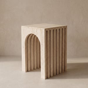 May include: A beige, square side table with an arched opening and vertical, grooved detailing. The table is made of a stone-like material and has a minimalist design. The table is approximately 18 inches tall.