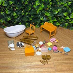 May include: A collection of miniature dollhouse accessories including a white bathtub, a yellow chair, a yellow bench, a small black and white rabbit figure, an orange handbag, a pink handbag, various small food items, plates, and gold-colored hardware pieces.