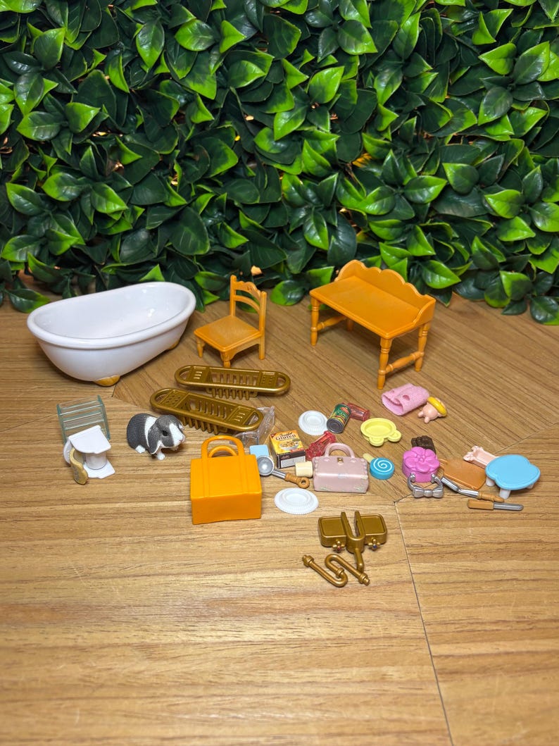 May include: A collection of miniature dollhouse accessories including a white bathtub, a yellow chair, a yellow bench, a small black and white rabbit figure, an orange handbag, a pink handbag, various small food items, plates, and gold-colored hardware pieces.