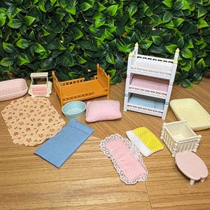 May include: A collection of miniature dollhouse furniture and accessories including a three-tier white bunk bed, an orange bed frame, a small white crib, a pink table, various fabric bedding pieces with floral and polka dot patterns, and plastic trays.