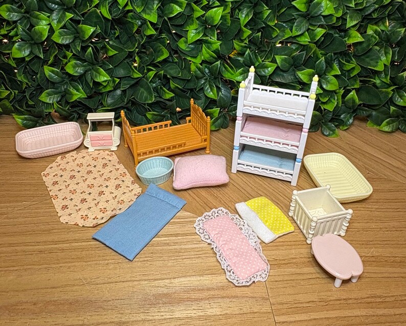 May include: A collection of miniature dollhouse furniture and accessories including a three-tier white bunk bed, an orange bed frame, a small white crib, a pink table, various fabric bedding pieces with floral and polka dot patterns, and plastic trays.