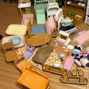 May include: A collection of miniature plastic dollhouse furniture and accessories, including a Food Corner shop stand, a bed with a pink pillow, a vanity, chairs, tables, a small bathtub, and various tiny household items in assorted colors.
