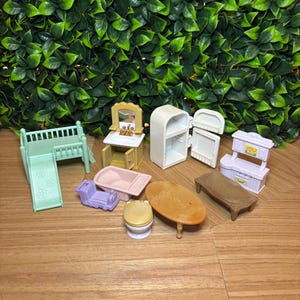 May include: A collection of miniature dollhouse furniture including a light green crib with a slide, a yellow vanity with a mirror, a white refrigerator, a pink bathtub, a purple toy train, a toilet, an oval wooden table, and a white kitchen unit.