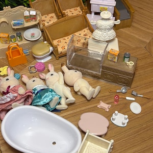 May include: A collection of miniature toy furniture and accessories including a white bathtub, a crib, two wooden benches with floral cushions, a shop counter, a cash register, and four flocked rabbit figures in various outfits and poses.