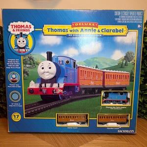 May include: A Thomas & Friends Deluxe Thomas with Annie & Clarabel HO scale electric train set box. The packaging features a blue Thomas the Tank Engine, orange Annie and Clarabel coaches, and a 36-inch circle of snap-fit E-Z track for assembly.