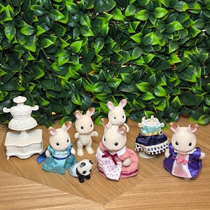 May include: A collection of flocked animal figurines including four rabbits and one small panda. The set features a white dress form on a stand, a blue dress, a pink dress with a white polka dot apron, and a purple dress with a pink panel.