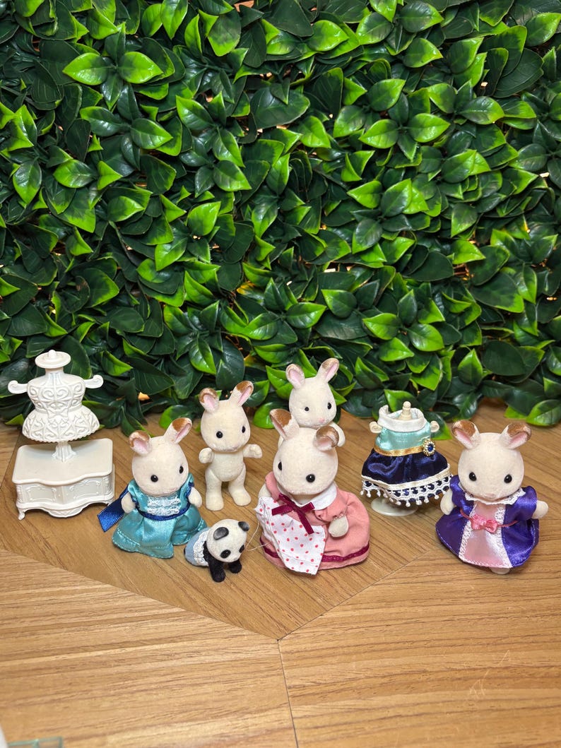 May include: A collection of flocked animal figurines including four rabbits and one small panda. The set features a white dress form on a stand, a blue dress, a pink dress with a white polka dot apron, and a purple dress with a pink panel.