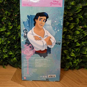 May include: A Disney Princess Prince classic doll box. The box features a cartoon illustration of Prince, with the text "Prince" and "Classic Doll" in English and French. The Disney Princess logo is visible.