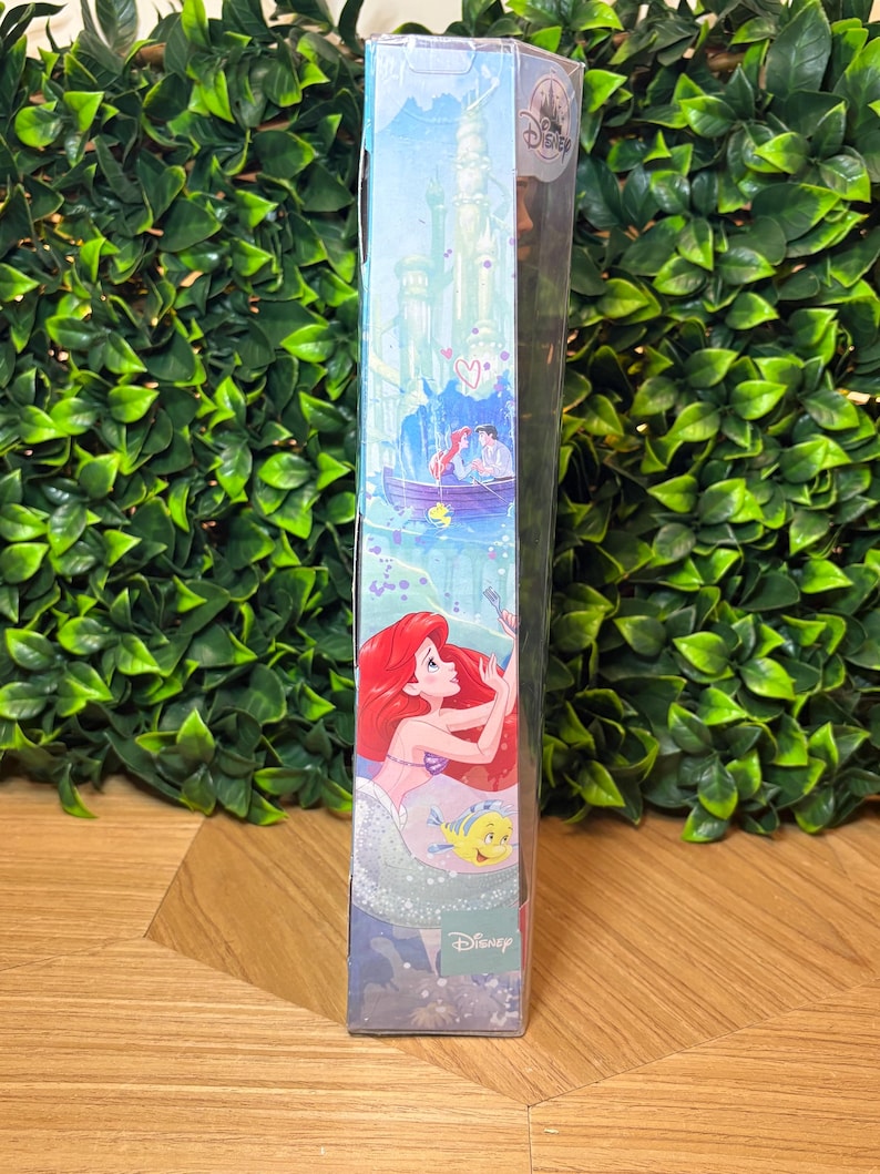 May include: A Disney-themed box featuring illustrations of Ariel, Prince Eric, and Flounder. The box has a light blue background with a castle and boat scene. The Disney logo is visible.