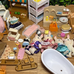 May include: A collection of miniature dollhouse furniture and animal figures, including a food corner stand, a white triple-bunk bed, a bathtub, and several rabbit figures dressed in fabric clothing, alongside various small accessories like bags and food items.