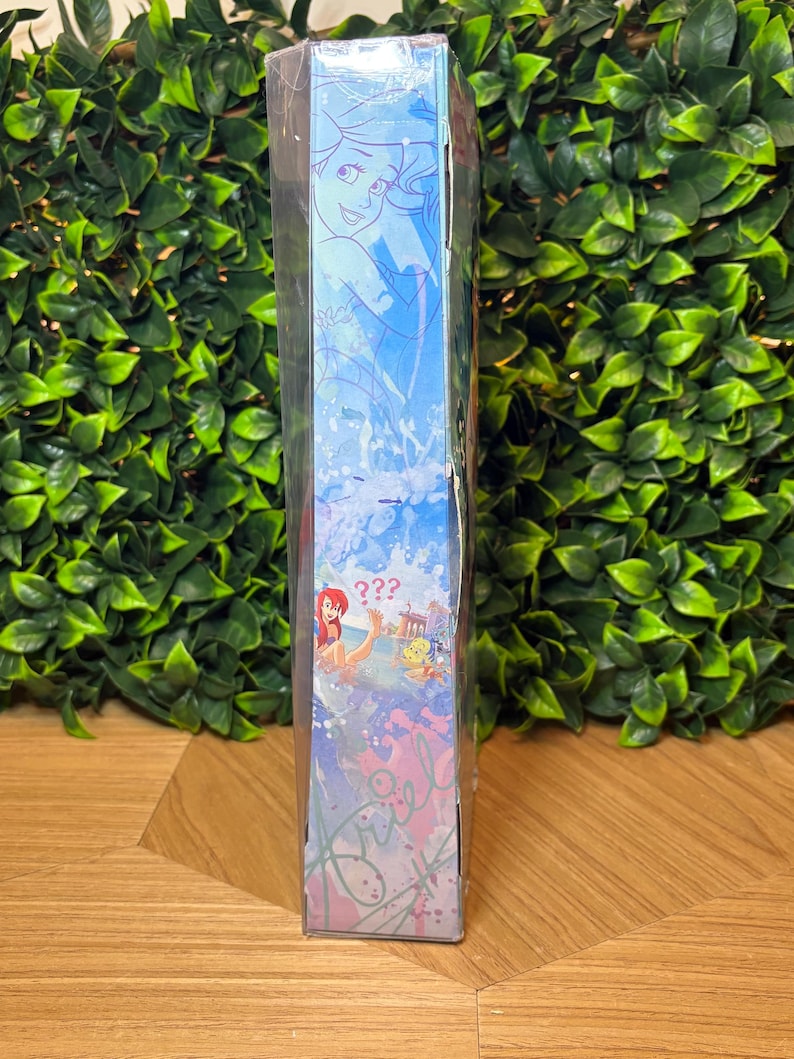 May include: A blue box featuring illustrations of Ariel from The Little Mermaid. The box has a light blue background with images of Ariel and other characters. The text "???" is visible on the box.