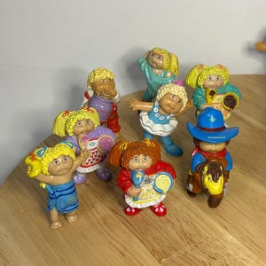 Peut inclure: Collection de figurines vintage Cabbage Patch Kids. Les poupées ont des cheveux blonds ou roux et portent diverses tenues, dont des robes, un chapeau de cow-boy et un maillot de bain bleu. Certaines tiennent des accessoires comme un cookie ou une sucette.