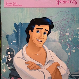 May include: A Disney Princess Prince Eric classic doll box. The box features a smiling Prince Eric illustration in a white shirt with crossed arms. The Disney Princess logo is visible, along with a drawing of Ariel.