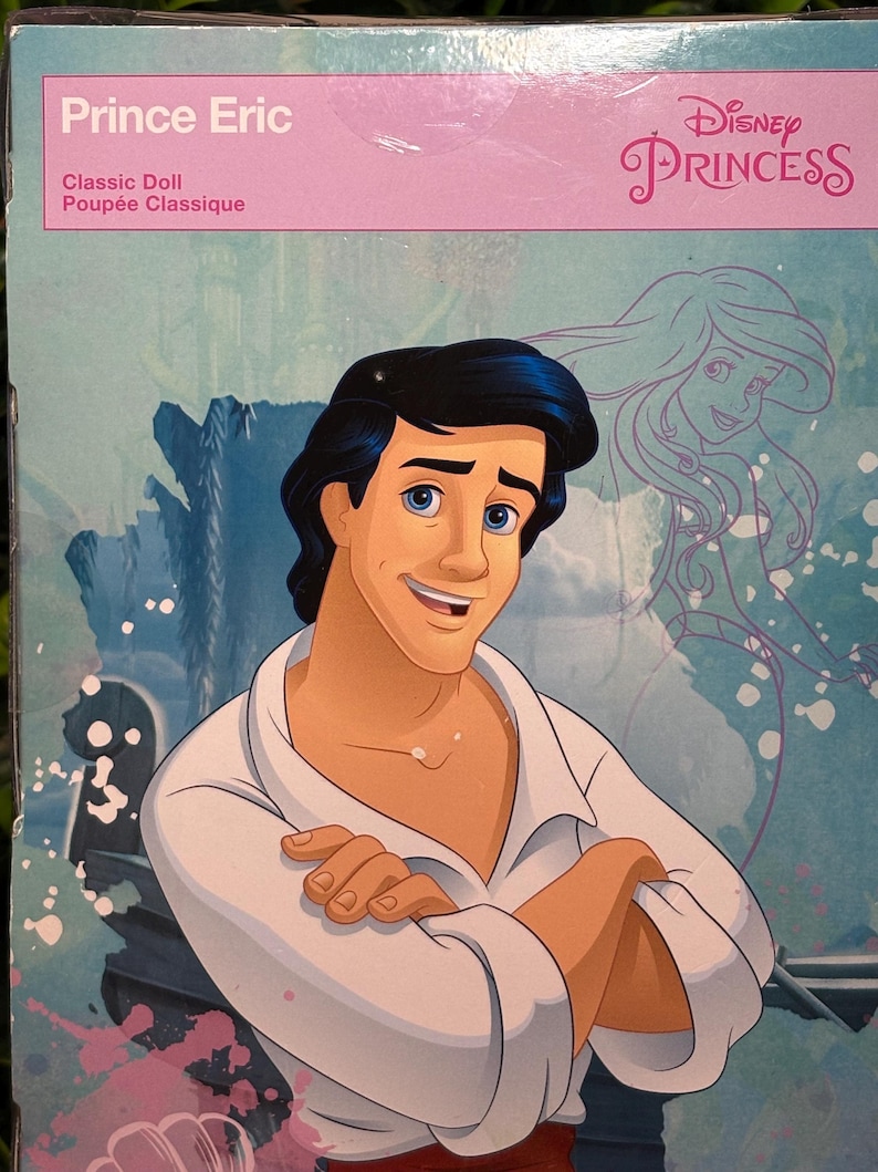 May include: A Disney Princess Prince Eric classic doll box. The box features a smiling Prince Eric illustration in a white shirt with crossed arms. The Disney Princess logo is visible, along with a drawing of Ariel.