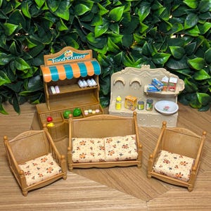 May include: A miniature toy set featuring a brown Food Corner shop stand with an orange and teal striped awning, a beige kitchen unit with various food accessories, and three brown chairs with cream-colored cushions featuring a small floral pattern.