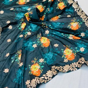 May include: Dark teal fabric with a floral pattern featuring orange and yellow blooms and teal accents. The fabric has a gold embroidered border with floral designs and small white flower accents scattered across the surface.