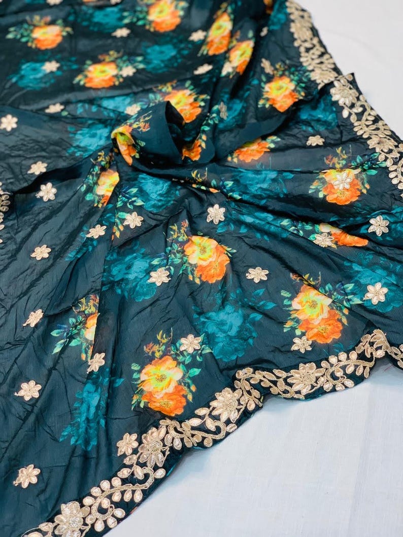 May include: Dark teal fabric with a floral pattern featuring orange and yellow blooms and teal accents. The fabric has a gold embroidered border with floral designs and small white flower accents scattered across the surface.